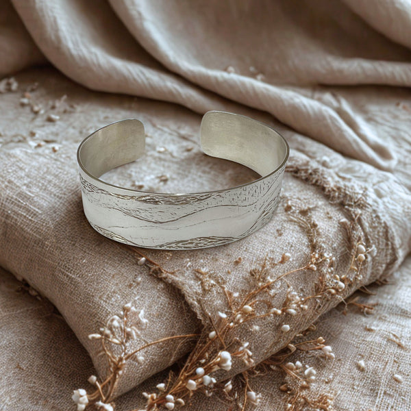 Silver cuff bracelet on a textured beige fabric background with dried flowers.