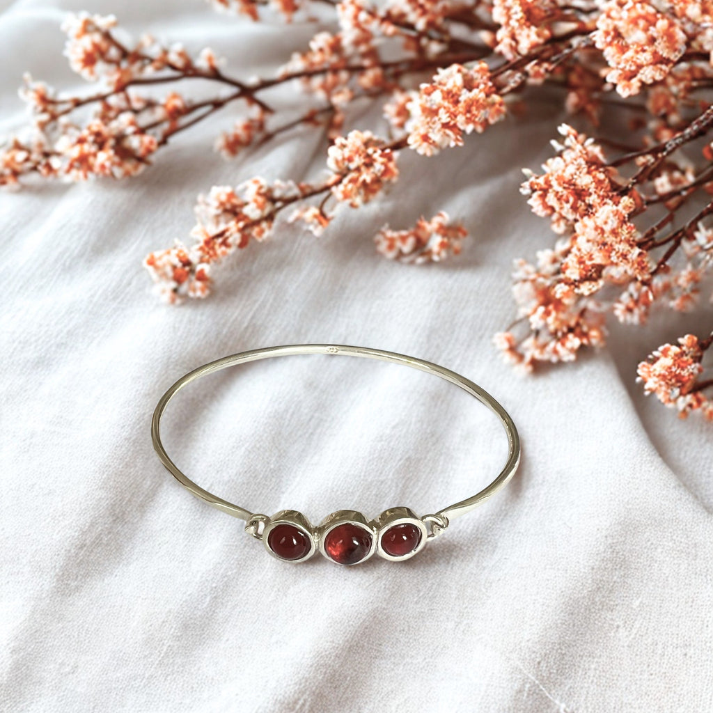Silver bracelet with red stones on a white fabric background with pink flowers