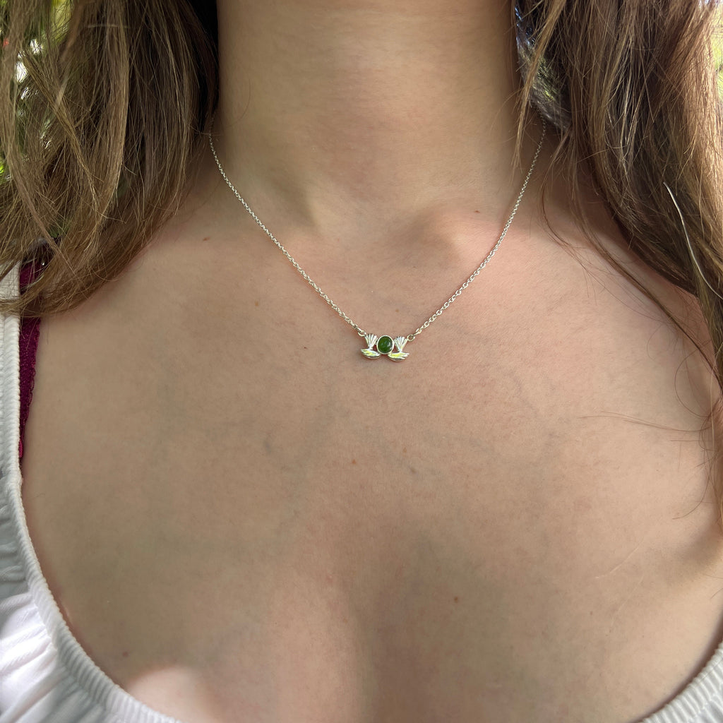 Close-up of a necklace with a green gemstone on a person wearing a white sleeveless top.