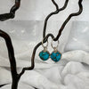 Turquoise earrings on a decorative branch against a textured white background