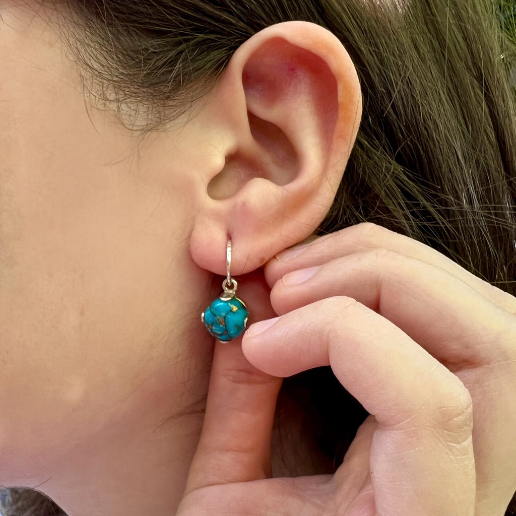Close-up of an ear with a turquoise earring being adjusted by a hand.