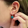 Close-up of an ear with a turquoise earring being adjusted by a hand.