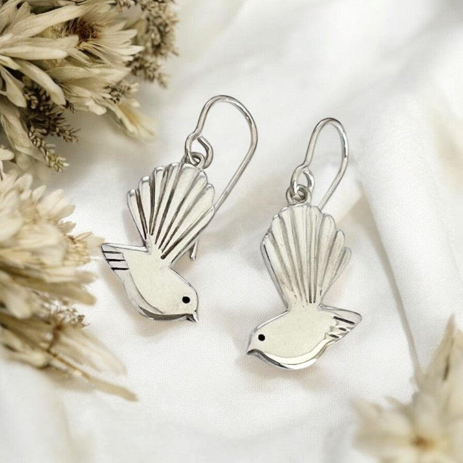 Silver bird-shaped earrings on a white background with dried flowers.