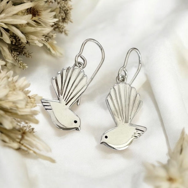 Silver bird-shaped earrings on a white background with dried flowers.
