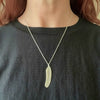 Person wearing a necklace with a feather shaped pendant on a plain background