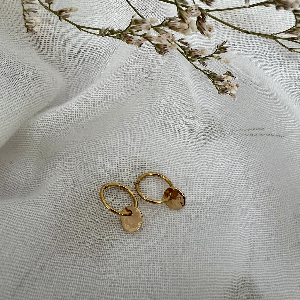 Gold earrings on a textured white fabric background with dried flowers.