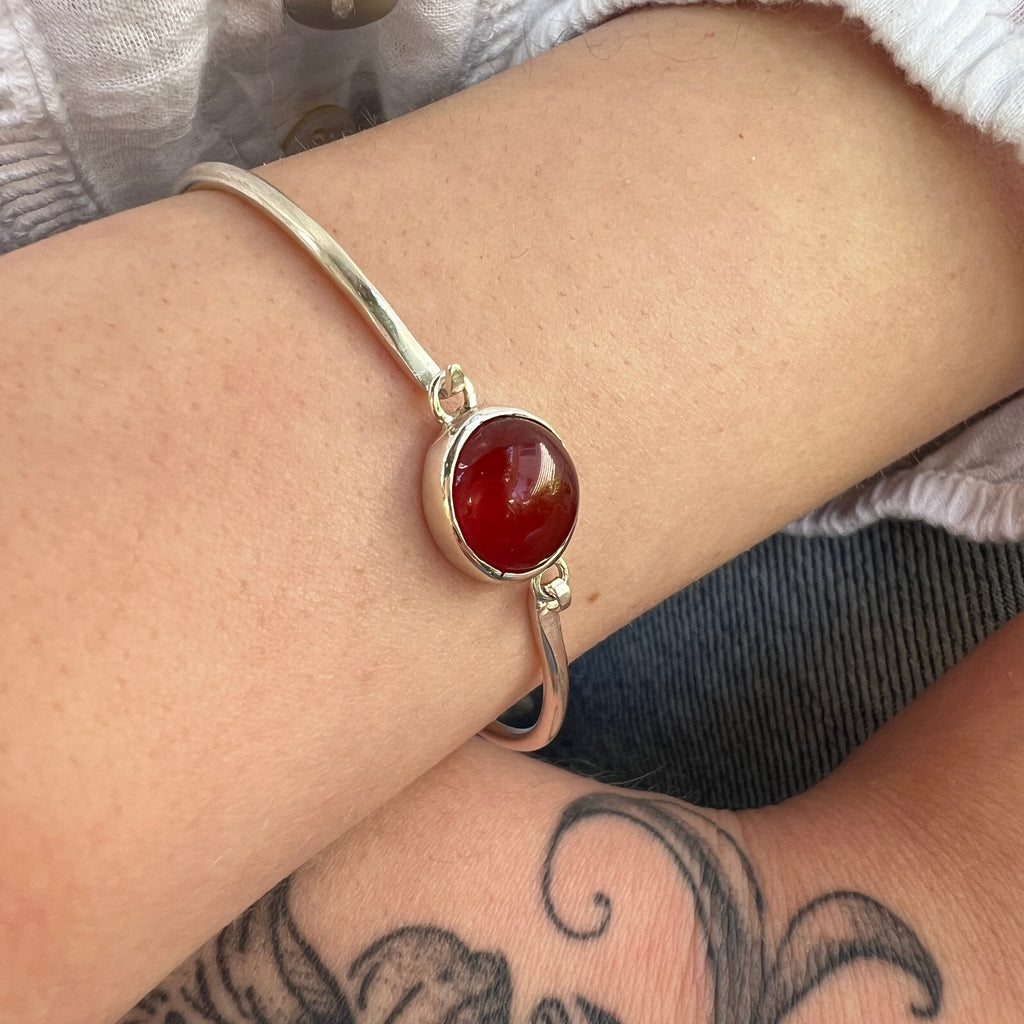 Silver bracelet with a red stone on a wrist with tattoos