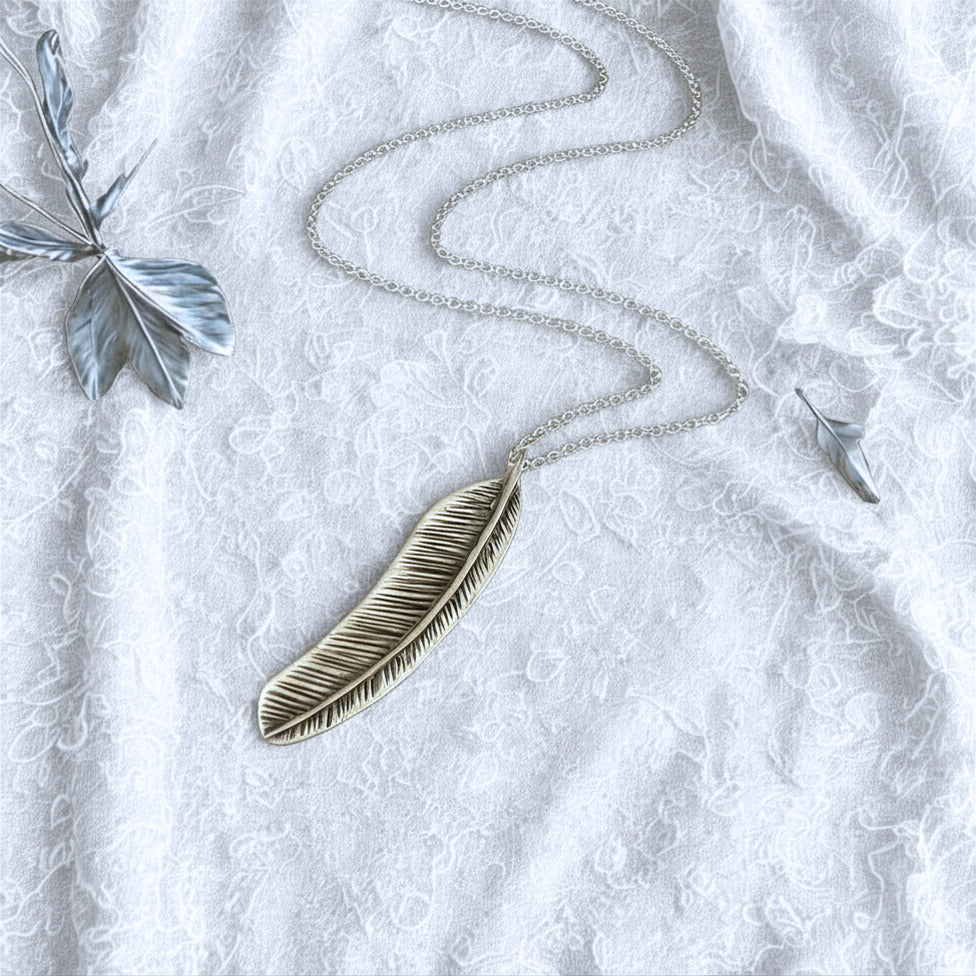 Silver feather necklace on a textured white surface with decorative elements.