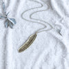 Silver feather necklace on a textured white surface with decorative elements.