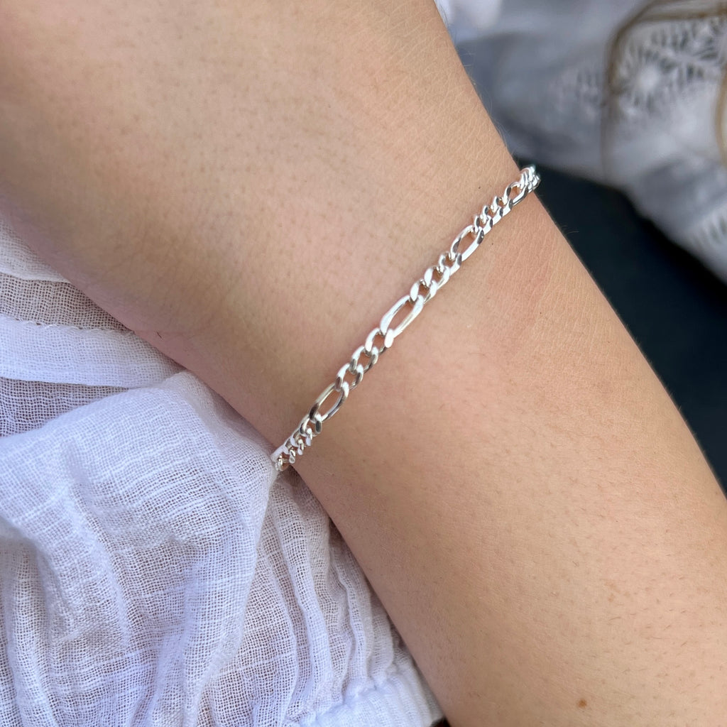 Silver chain bracelet on a wrist with a white fabric background.