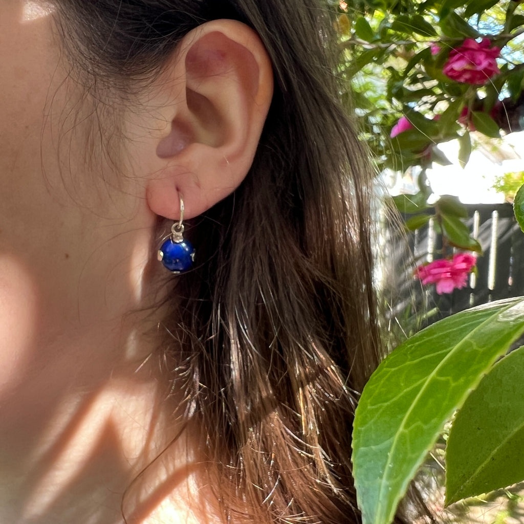 Close-up of an ear wearing a blue earring with flowers in the background