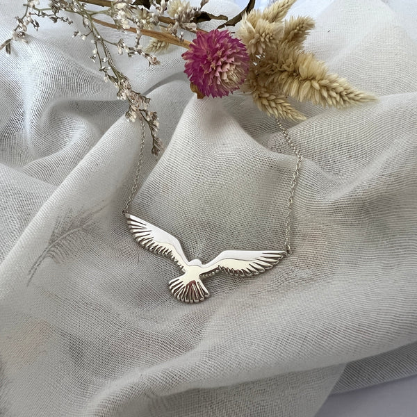 Silver bird-shaped pendant on a textured fabric background with dried flowers.