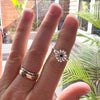 Hand wearing two silver rings with a black stone, set against a blurred outdoor background.