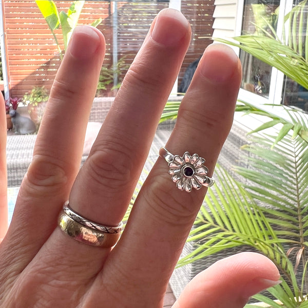 Hand wearing two silver rings with a black stone, set against a blurred outdoor background.