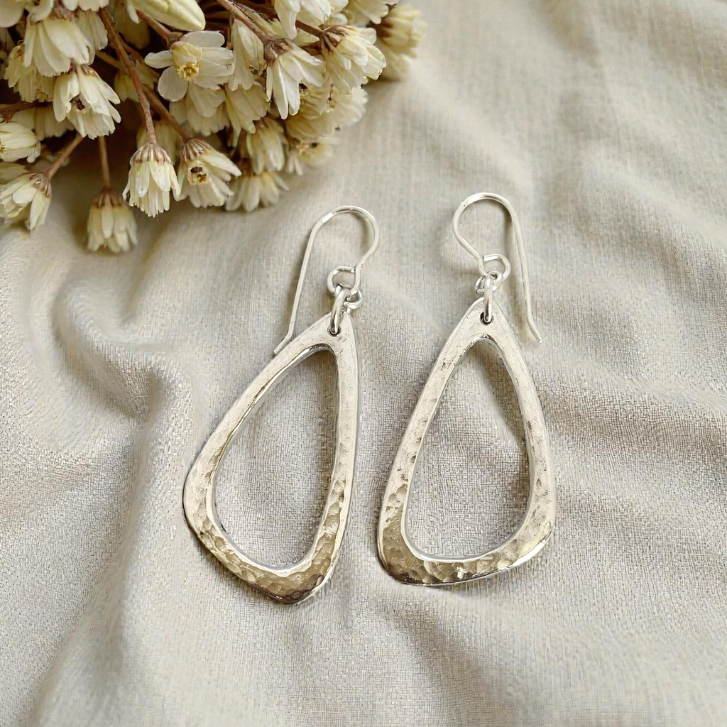 Silver teardrop earrings on a beige fabric background with dried flowers.
