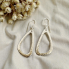 Silver teardrop earrings on a beige fabric background with dried flowers.