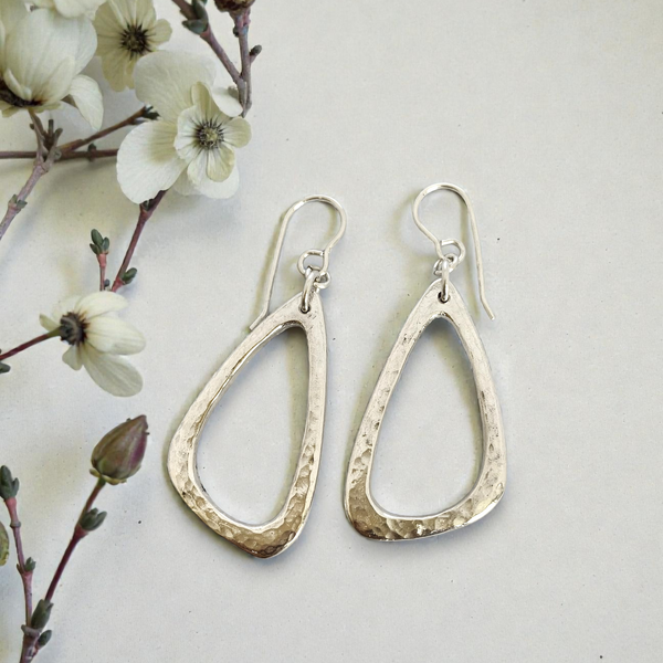 Silver teardrop earrings on a light background with white flowers.