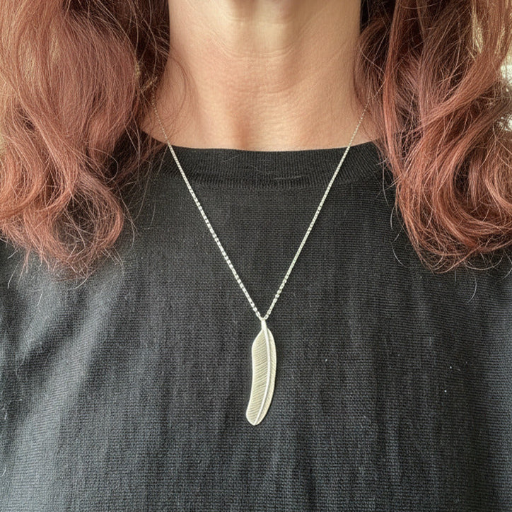 Person wearing a silver necklace with a pendant against a neutral background