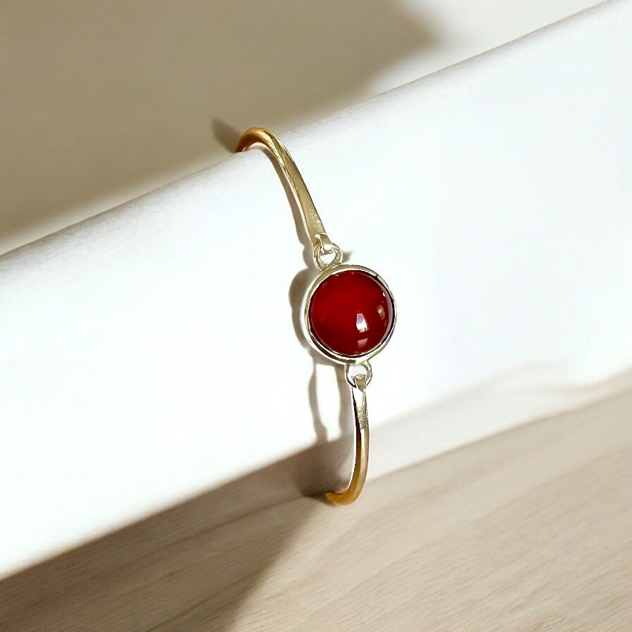 Silver bracelet with red stone on a light wooden surface.