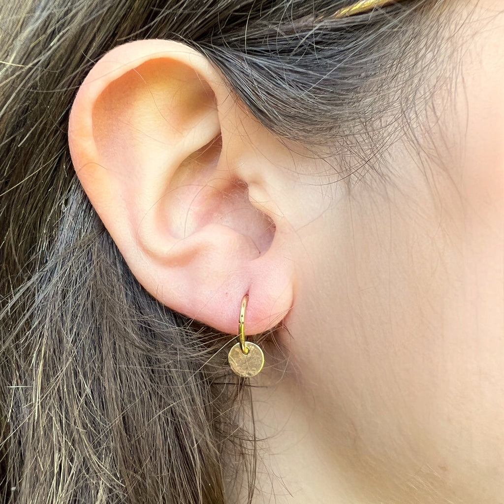 Close-up of an ear wearing a gold hoop earring with a blurred background