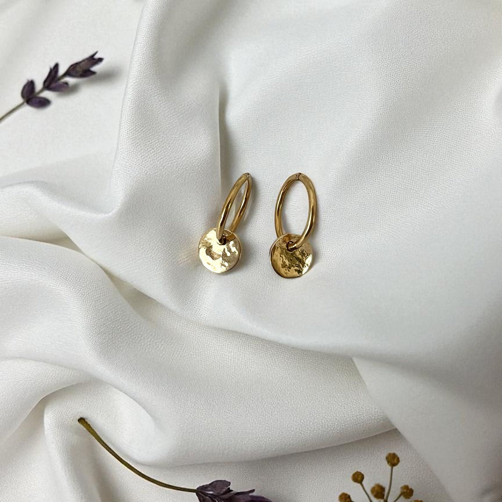 Gold hoop earrings on a white fabric background with dried flowers.