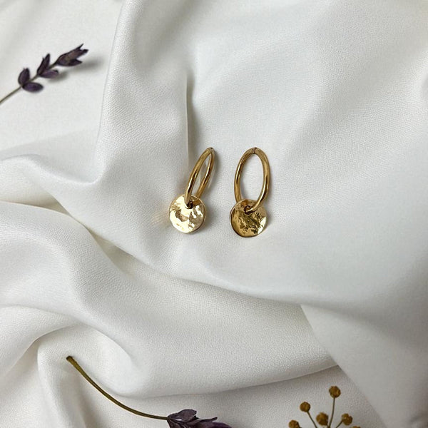 Gold hoop earrings on a white fabric background with dried flowers.