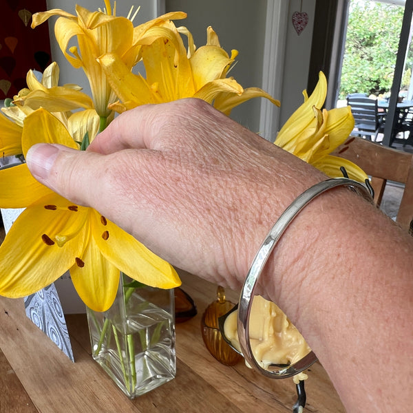 Hand holding yellow flowers with a silver bracelet on a wooden surface