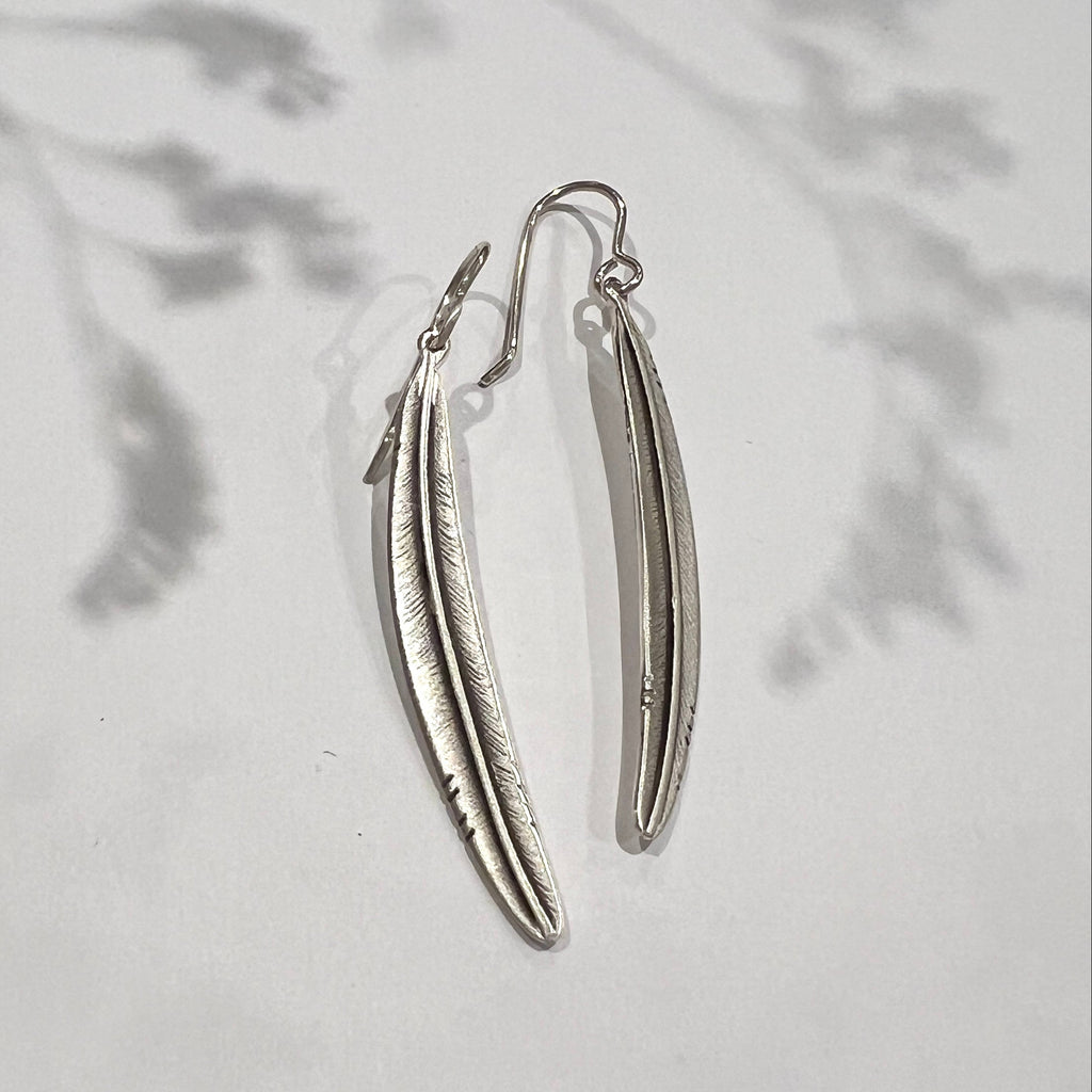 Silver feather-shaped earrings on a light gray background