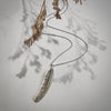 Silver feather necklace on a light gray background with dried leaves.