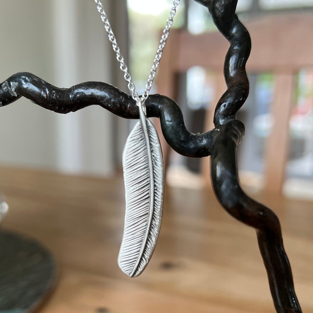Silver feather pendant necklace on a blurred background