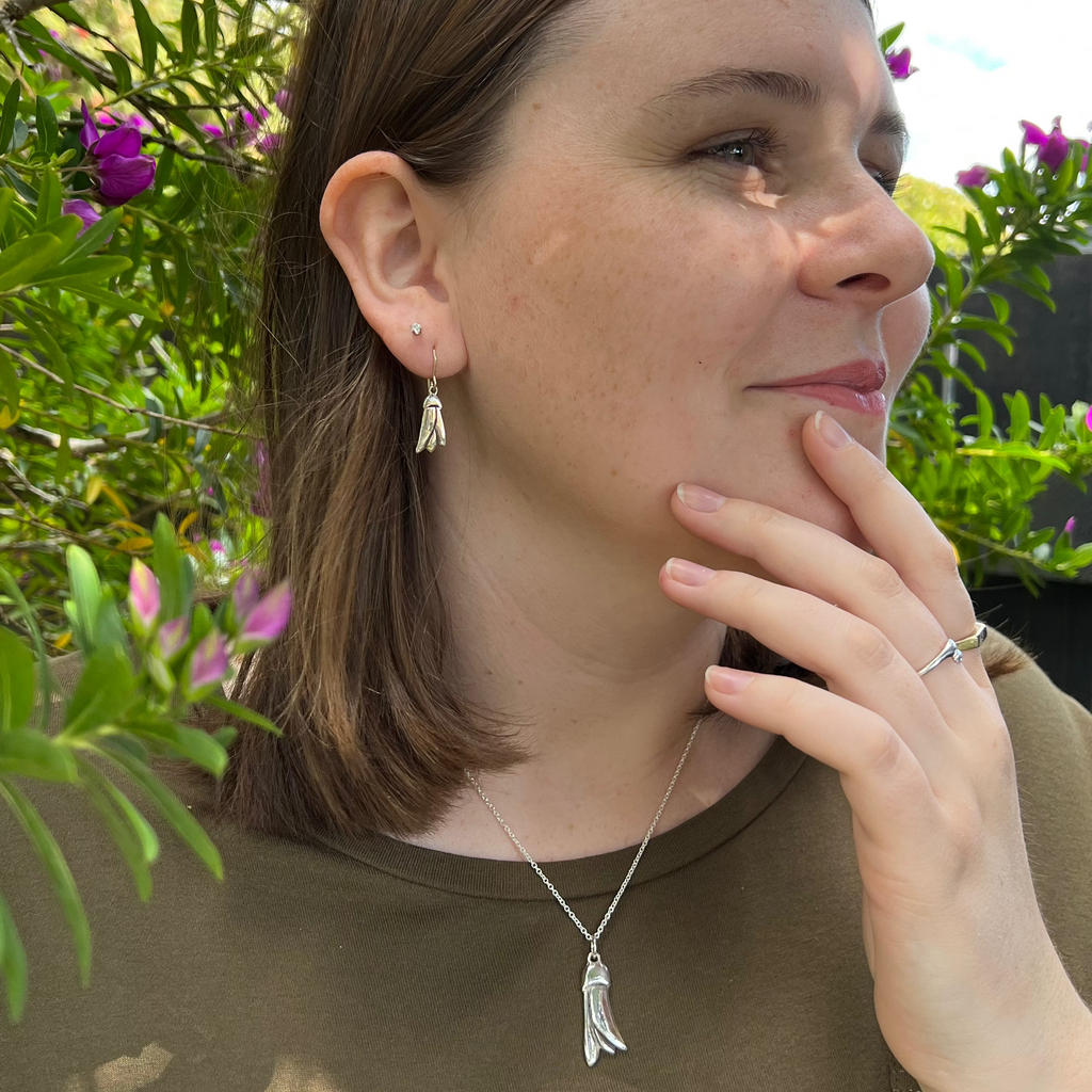 Woman wearing a necklace and earrings outdoors with greenery in the background