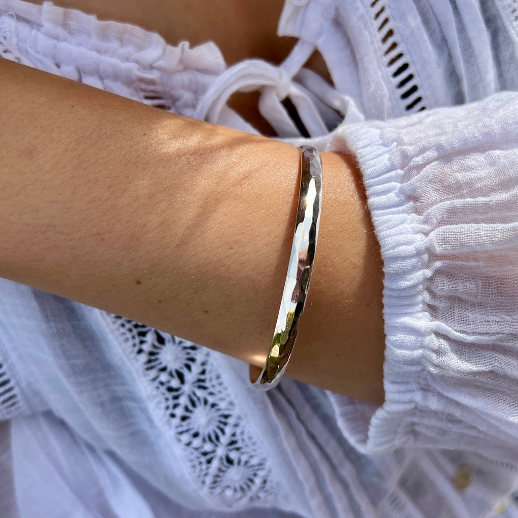 Silver bracelet on a wrist with a white lace garment in the background