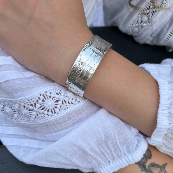 Silver bracelet on a wrist with a white lace garment and tattoo in the background
