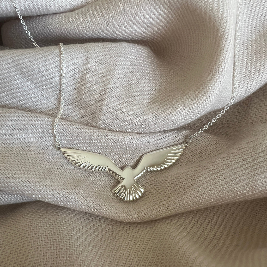Silver cook's petrel necklace resting on fabric background