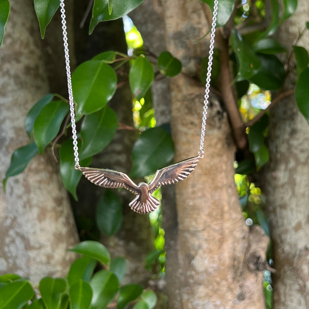 Bronze eagle pendant on a chain against a natural background of green leaves and tree bark.