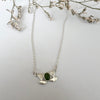 Silver necklace with a green gemstone pendant on a light gray background