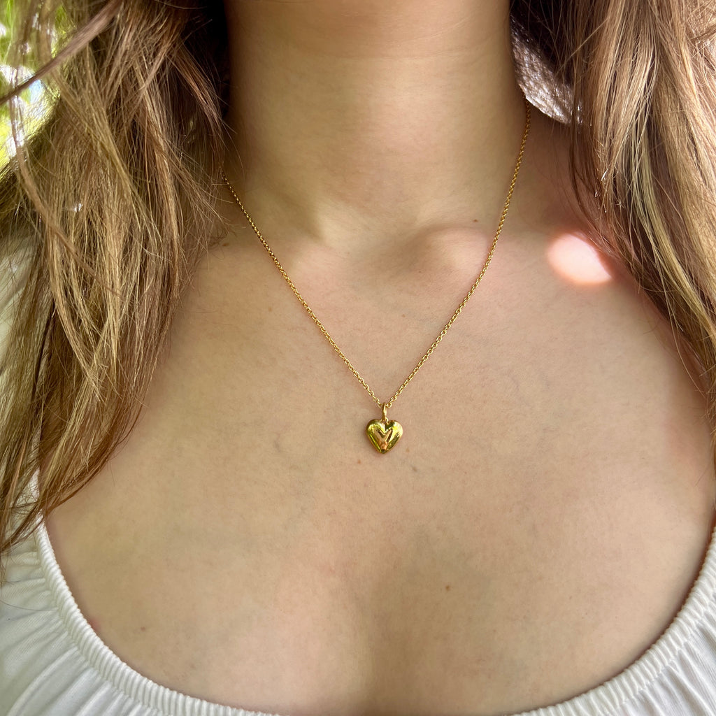 Gold heart-shaped necklace on a person wearing a white top.