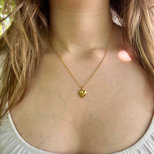 Gold heart-shaped necklace on a person wearing a white top.