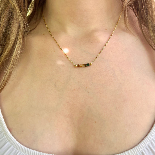 Necklace with small beads worn by a person with blonde hair, wearing a white top.