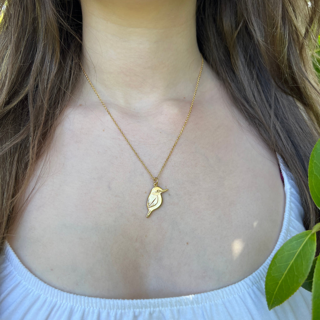 Gold bird necklace worn by a person with green leaves in the background