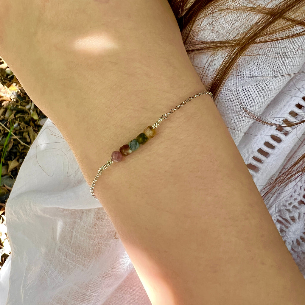 Close-up of a hand wearing a bracelet with multicolored beads, outdoors.