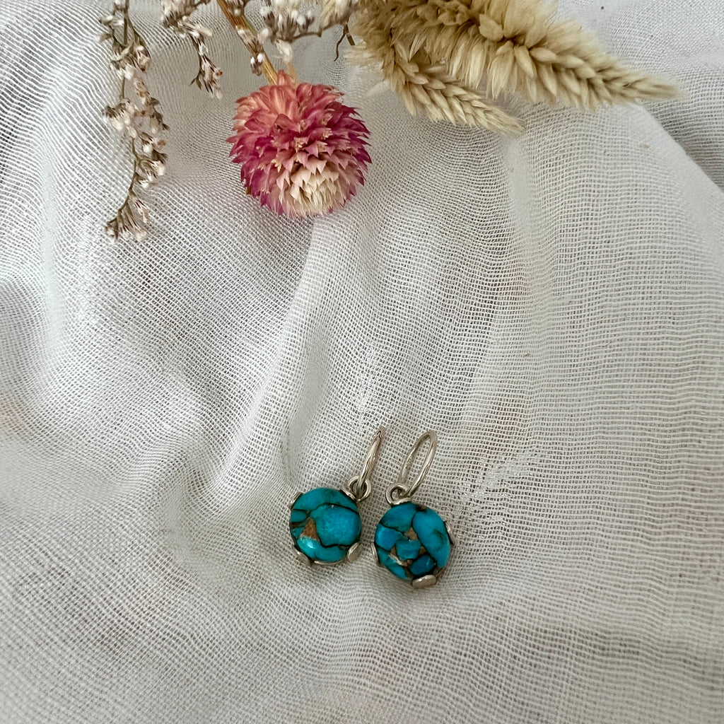 Turquoise earrings on a textured fabric background with dried flowers.