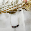 Silver ecklace with colored beads on a white fabric background with dried flowers.