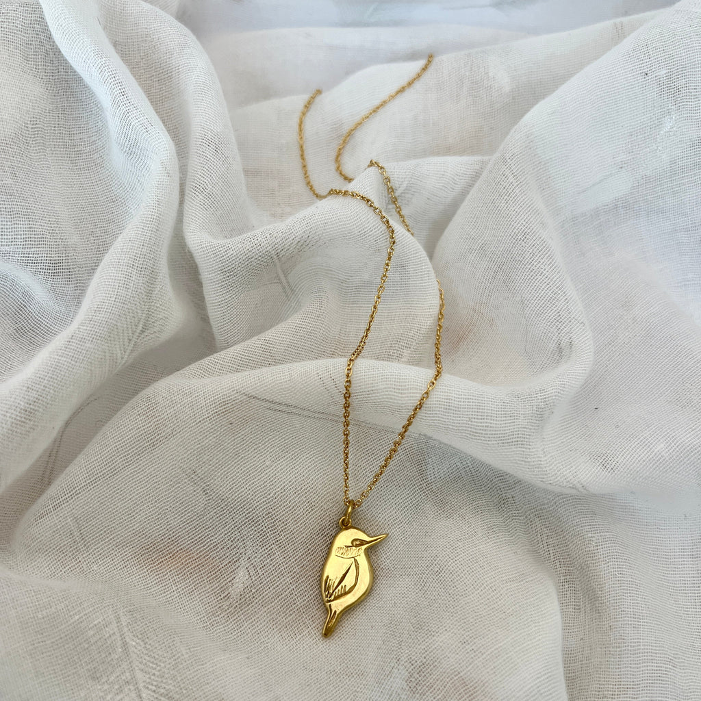 Gold necklace with a bird pendant on a white fabric background