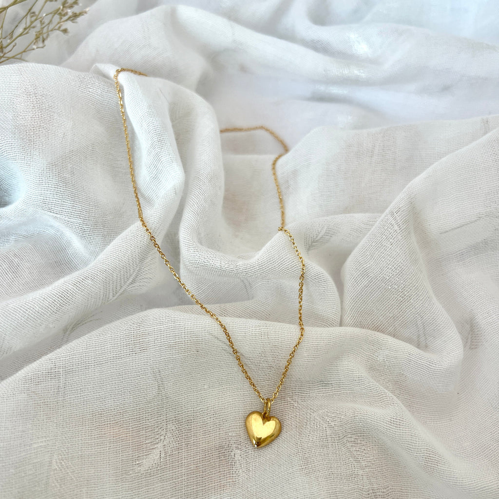 Gold heart-shaped necklace on a textured white fabric background