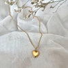 Gold heart-shaped pendant necklace on a white fabric background with dried flowers.