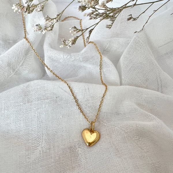 Gold heart-shaped pendant necklace on a white fabric background with dried flowers.