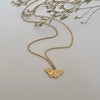 Gold butterfly necklace on a light gray background with dried flowers.