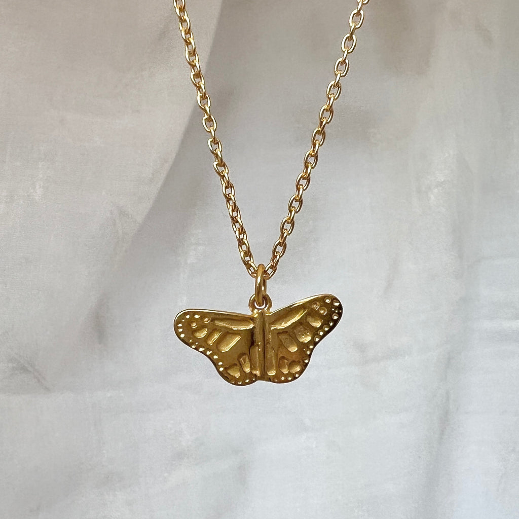 Gold butterfly necklace on a light gray background