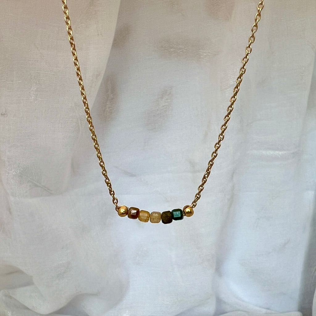 Necklace with small beads on a gold chain against a white fabric background